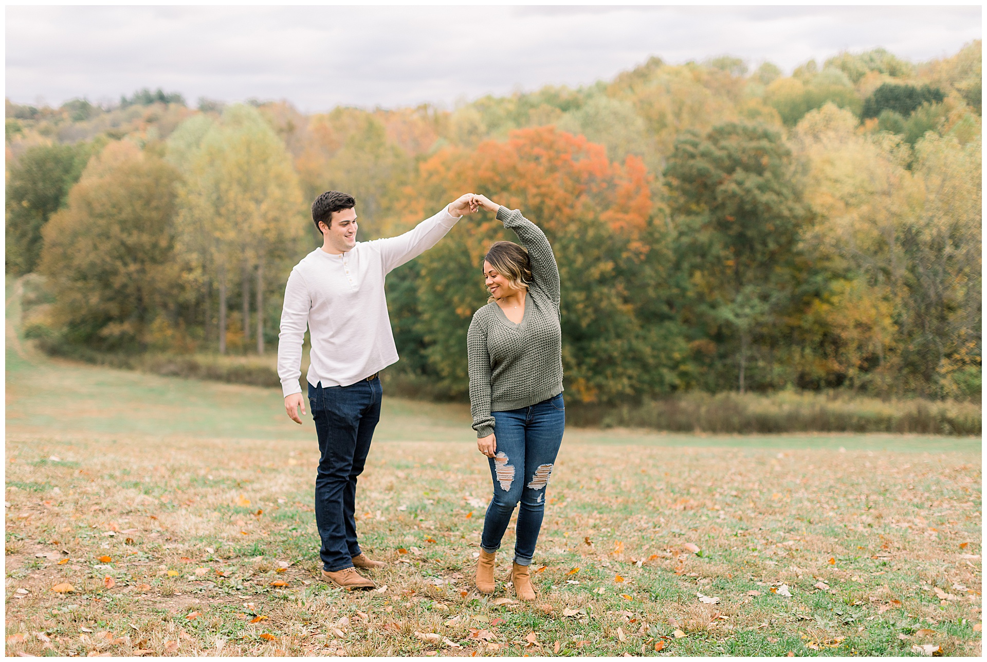 engaged couple twirls on top of a hill in a park during fall