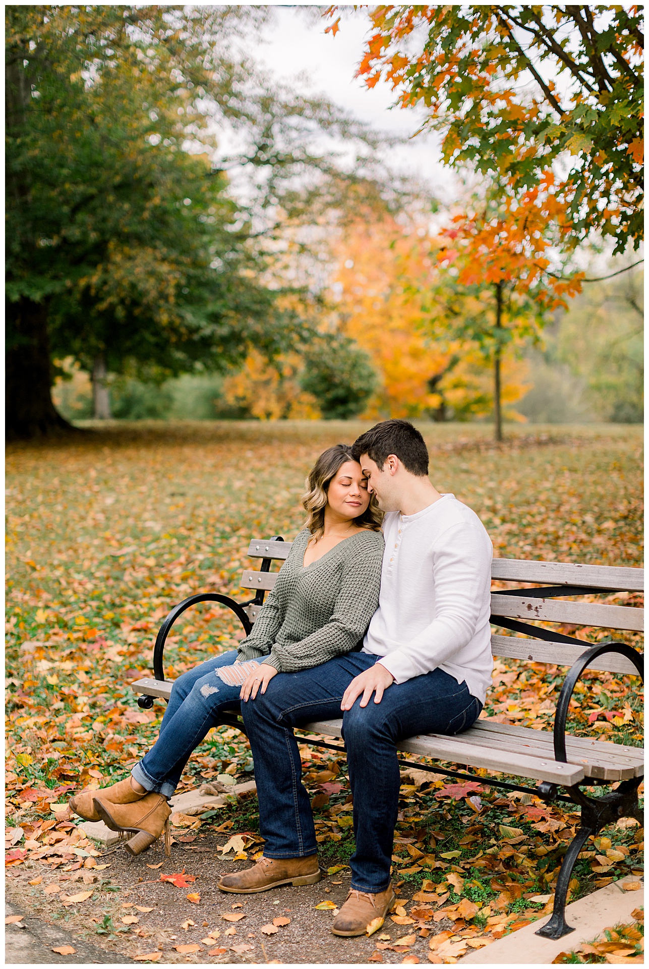 fall north carolina engaged couple sit on bench with colorful fall leaves